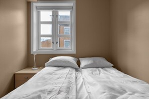 A single bed with white bedding in a room with beige walls and a window.