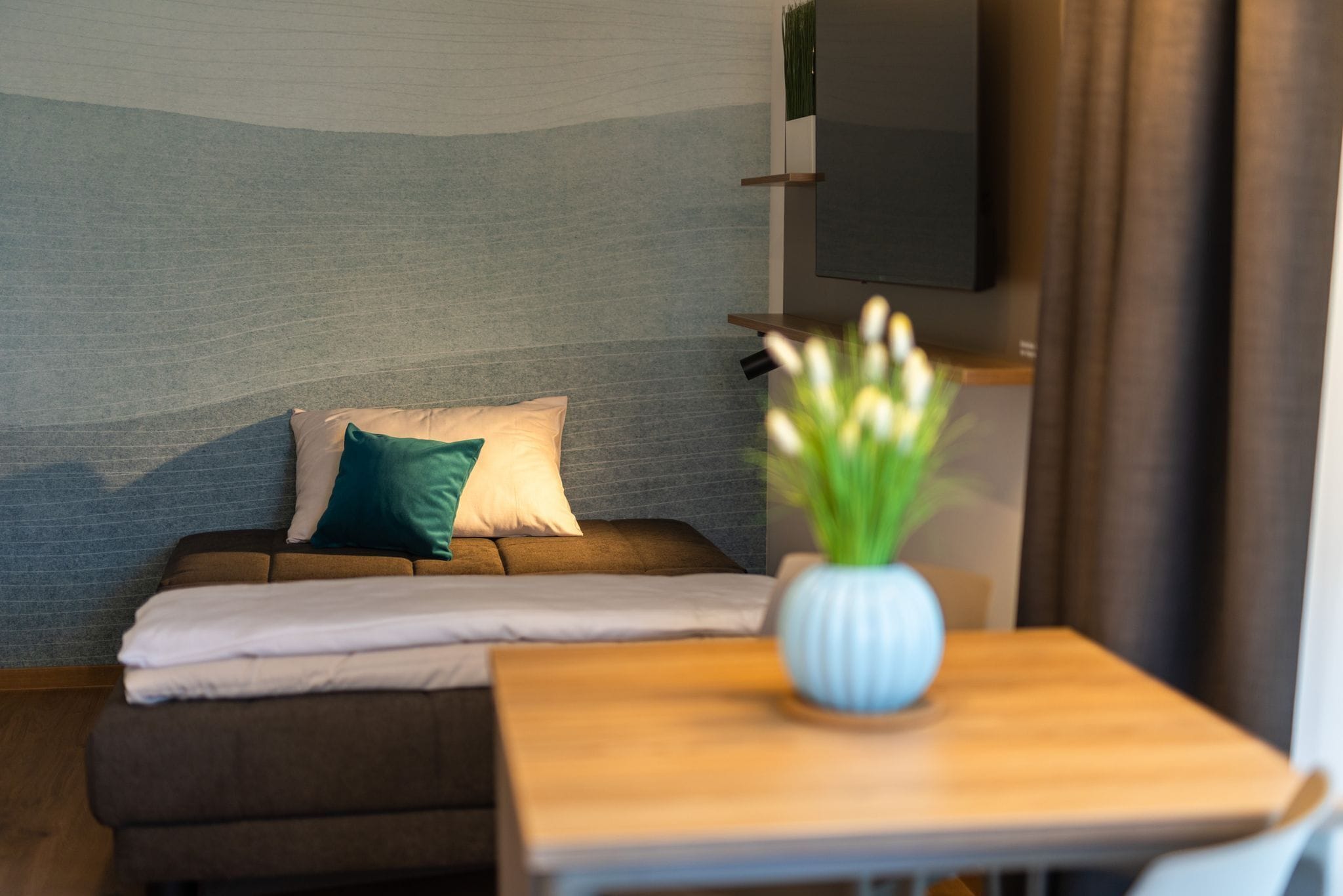 A cozy room with a sofa, pillows, a small table, and a TV mounted on the wall.