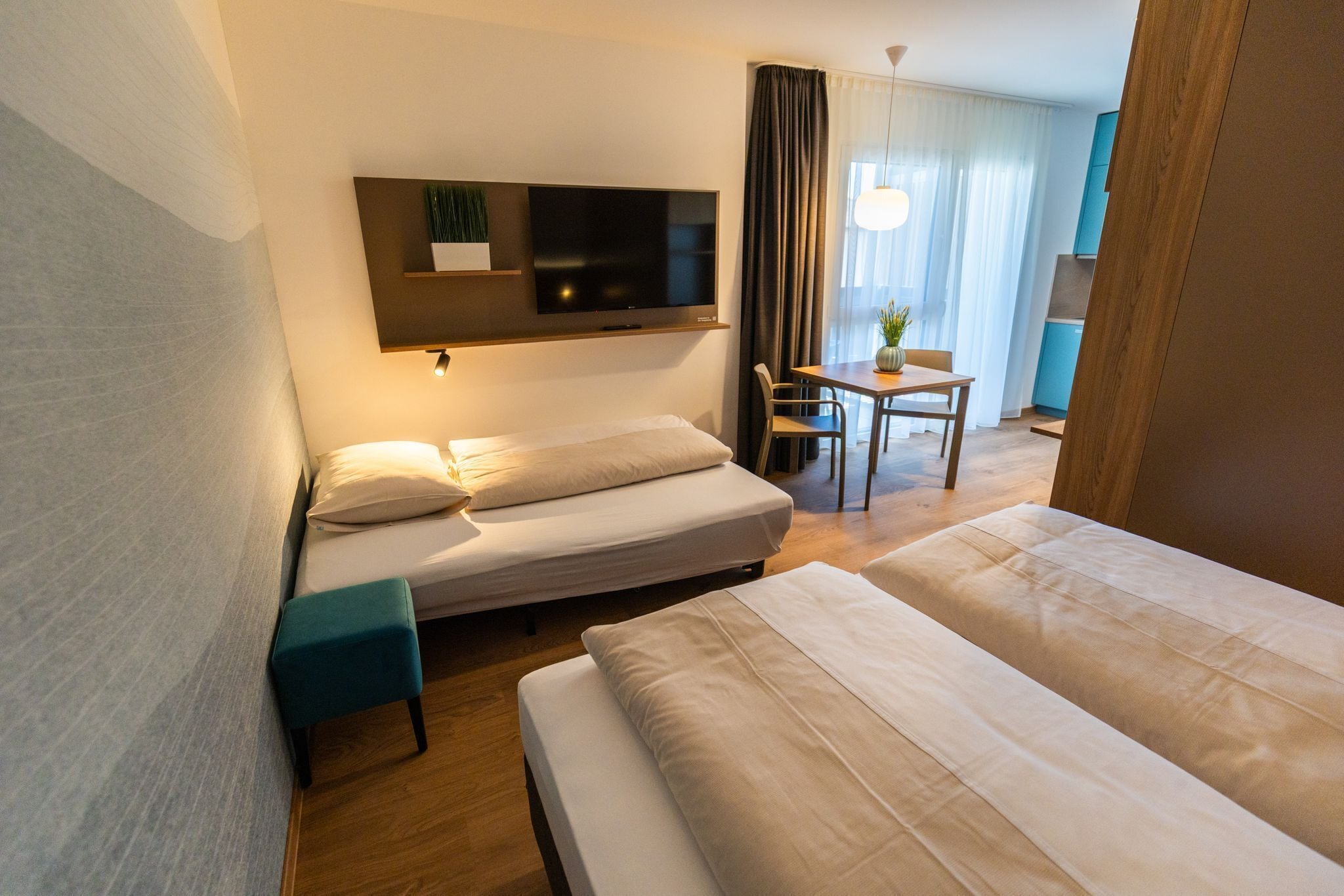 A hotel room with two beds, a desk, a chair, a TV, and a window with curtains.