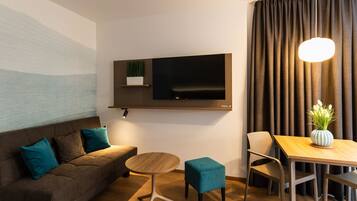 Un salon moderne comprenant un canapé, une table basse, un téléviseur fixé au mur et un coin repas avec une table et des chaises.