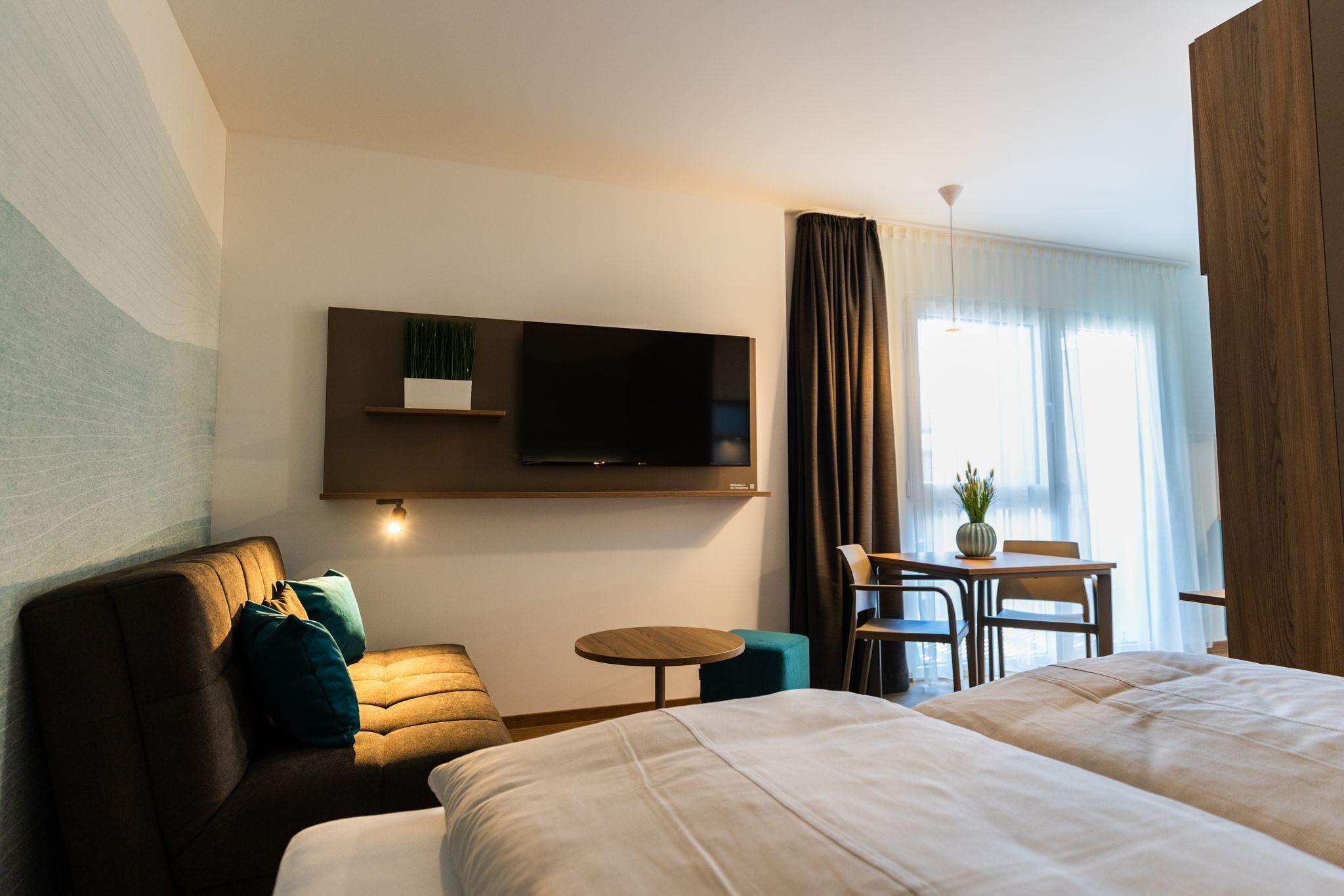 Habitació d'hotel amb un sofà, dos llits, un televisor fixat a la paret, una taula petita i una cadira.