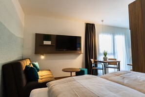 Een hotelkamer met een bank, twee bedden, een aan de muur bevestigde televisie, een tafeltje en een stoel.
