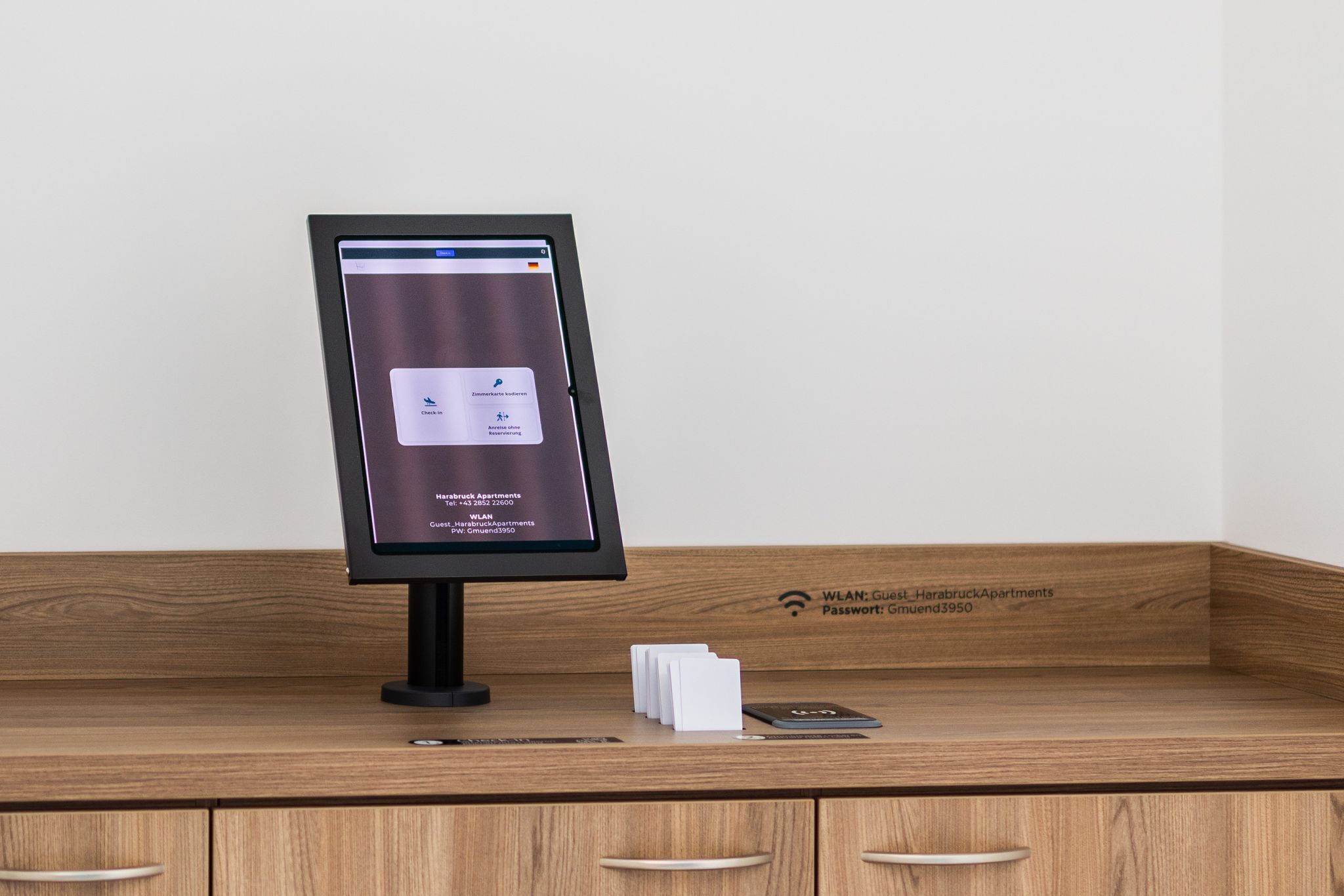 Un chiosco digitale con uno schermo che mostra informazioni e uno smartphone su un bancone in legno.