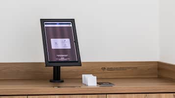 En digital informationskiosk med en skärm som visar information och en smartphone på en trädisk.
