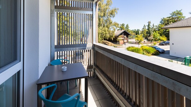 A balcony with a table and chairs, a wooden fence, and a view of a residential area with houses and cars.