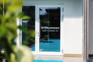 Een glazen deur met een welkomstbord en uitzicht op het zwembad.