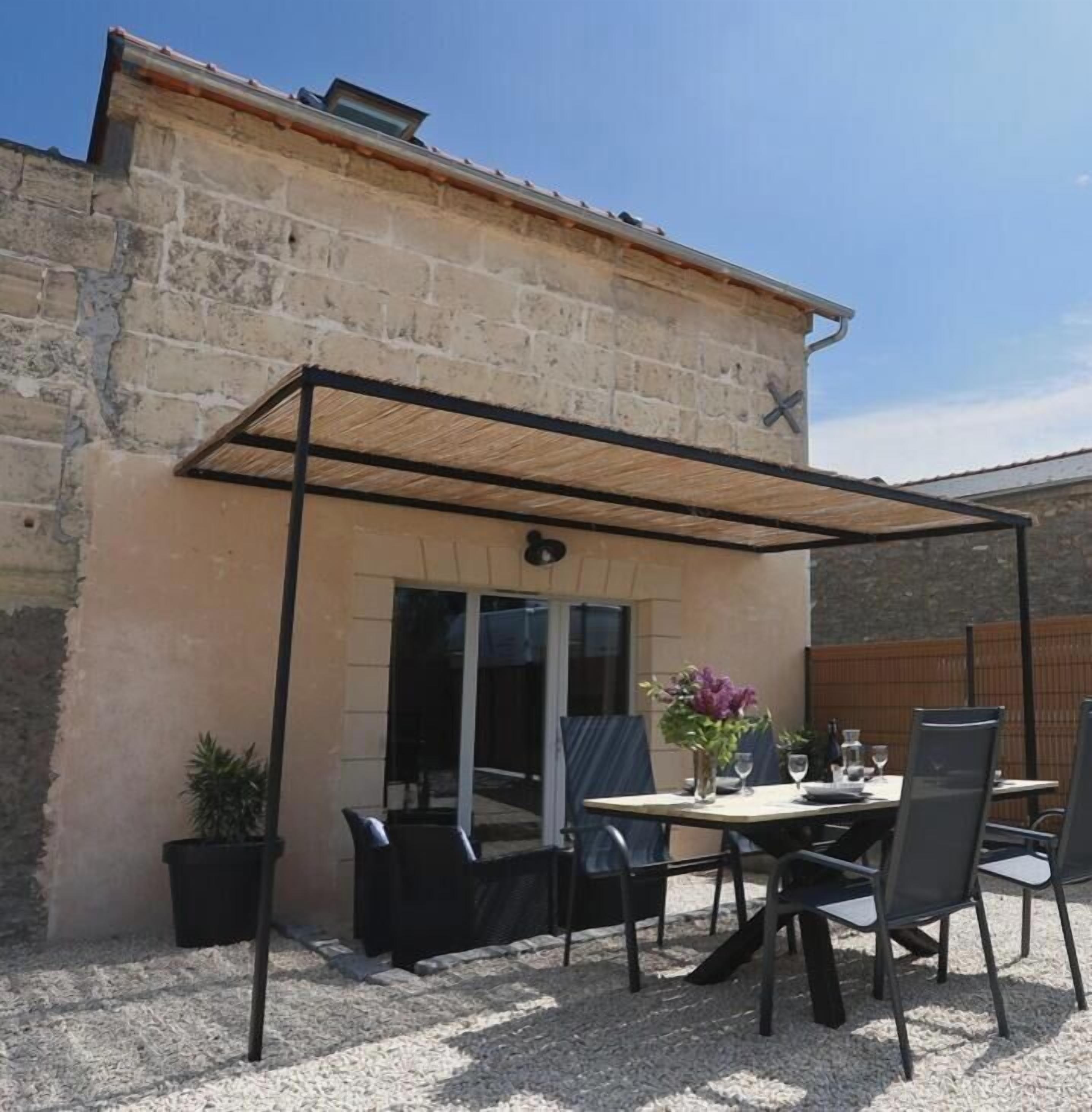 A patio area with a table and chairs, a covered seating area, and a stone building with a tiled roof.