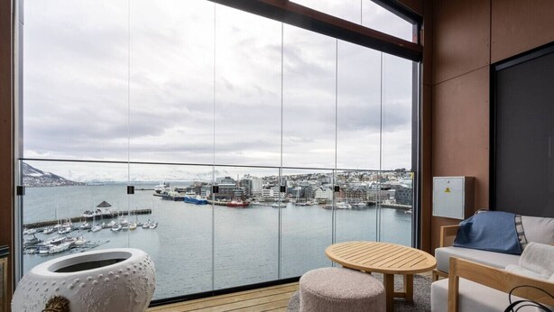 A modern room with a large window, a round wooden table, a sofa, and a decorative white urn. - Northstay - Polar Night I Exclusive Arctic Penthouse (Tromsø)
