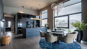 A modern kitchen with a central island, a dining area with a round table, and large windows offering a view of a snowy landscape. - Northstay - Polar Night I Exclusive Arctic Penthouse (Tromsø)