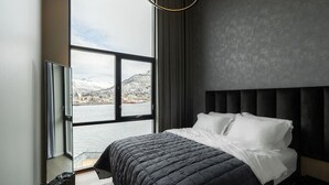 A bedroom with a large window, a bed with white bedding, and a dark headboard. - Northstay - Polar Night I Exclusive Arctic Penthouse (Tromsø)