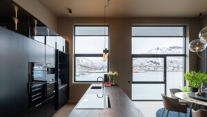 A modern kitchen with a marble island, large windows, and a view of a snowy landscape. - Northstay - Polar Night I Exclusive Arctic Penthouse (Tromsø)