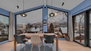 Ein zeitgemäßer Essraum mit einem großen Tisch, vier Stühlen und großen Fenstern mit Blick auf eine verschneite Landschaft.
