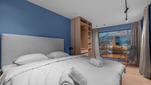 Ein Hotelzimmer mit einem großen Bett, einem Kleiderschrank, einem Sessel und Blick auf eine verschneite Landschaft.