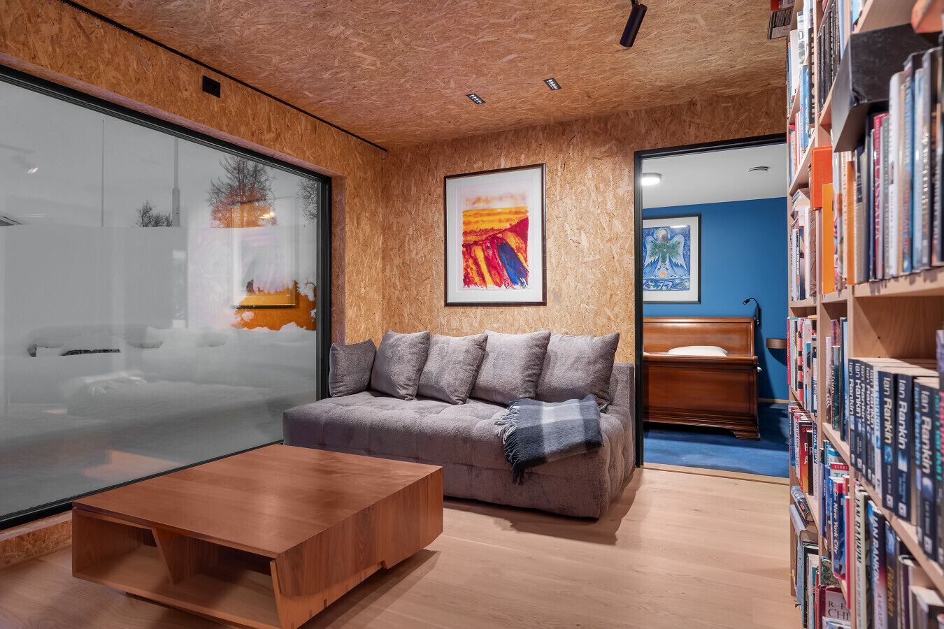 Een modern interieur met een houten plafond, een grijze bank, een houten salontafel en een boekenkast vol boeken.