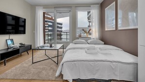 Ein modernes Hotelzimmer mit Bett, Schreibtisch, Fernseher und einem Balkon mit Blick auf Gebäude.