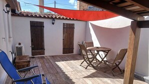 A patio with a wooden table and chairs, a blue folding chair, and a red canopy. - "La Plagette" Baraquette near Etang, Clim (Sète)