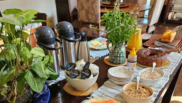 A breakfast table with various food items, a thermos, a bowl of berries, and a potted plant. - Villaggio Serra da Cantareira (Mairiporã)