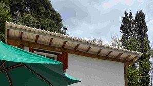 A two-story building with a patio area featuring lounge chairs and a green umbrella. - Villaggio Serra da Cantareira (Mairiporã)