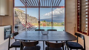 A dining area with a view of a pool and a stone wall. - Almoxarife Beach House (Horta)