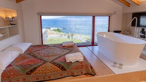 A bedroom with a large bed, a view of the sea, and a modern bathtub. - Almoxarife Beach House (Horta)