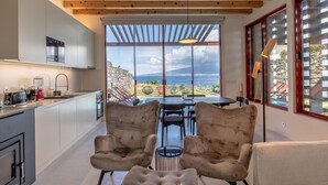 A modern kitchen with a view of the sea, a dining area with two chairs, and a large window. - Almoxarife Beach House (Horta)