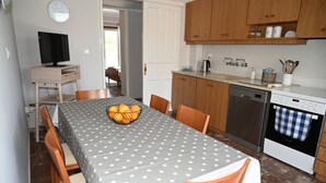 Cocina compacta con mesa, sillas, televisor en un mueble bajo y lavavajillas.