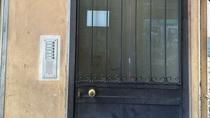 Una puerta negra con una reja metálica, un ventanal pequeño y un teclado electrónico.