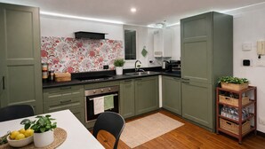 Una cocina compacta con armarios verdes, una encimera blanca, un horno empotrado y un pequeño comedor con mesa y sillas.