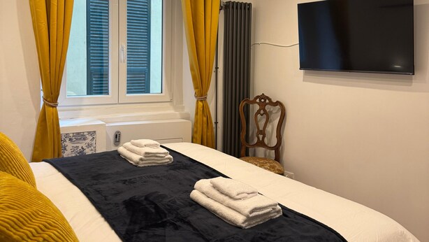 Una habitación de hotel con una cama, un televisor en la pared, una ventana con cortinas y un radiador.