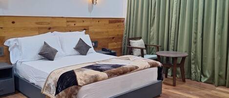 A bedroom with a wooden headboard, a bed with a blanket, a bedside table, a nightstand, a small round table, and a green curtain.
