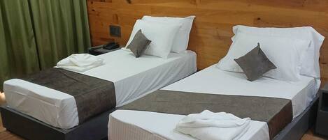 Two single beds with wooden headboards, a green curtain, and a small rug on a wooden floor.
