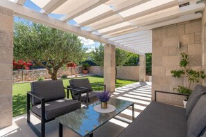 An outdoor patio with a glass table, two grey sofas, and a pergola structure. - Villa Korana with heated Pool and Jacuzzi (Kamenmost)
