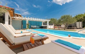 A pool area with lounge chairs, a pergola, and a clear blue sky. - Villa Korana with heated Pool and Jacuzzi (Kamenmost)