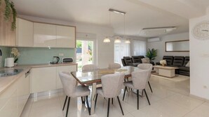 A modern kitchen with a dining area, a living room with a sofa, and a large window. - Villa Korana with heated Pool and Jacuzzi (Kamenmost)