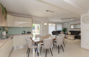 A modern kitchen with a dining area, a living room with a sofa, and a large window. - Villa Korana with heated Pool and Jacuzzi (Kamenmost)