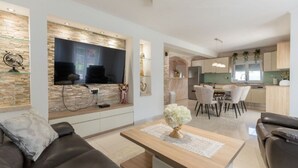 A modern living room with a flat-screen TV, a sofa, a coffee table, and a dining area with chairs and a table. - Villa Korana with heated Pool and Jacuzzi (Kamenmost)