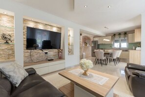 A modern living room with a flat-screen TV, a sofa, a coffee table, and a dining area with chairs and a table. - Villa Korana with heated Pool and Jacuzzi (Kamenmost)