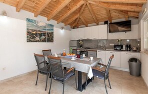 A dining area with a table set for four, surrounded by chairs, in a kitchen with white cabinets and a wooden ceiling. - Villa Korana with heated Pool and Jacuzzi (Kamenmost)