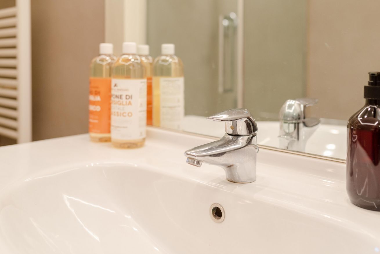 Un lavabo de salle de bain avec un robinet chromé, un miroir et trois bouteilles de savon liquide.