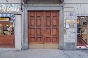 A double wooden door with a plaque, a 'no parking' sign, and a storefront with a sign that reads 'MARCO'.