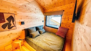 Una habitación de cabaña de madera con cama, ventana y un taburete pequeño.