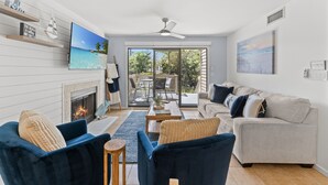 Ein Wohnzimmer mit Kamin, Fernseher, Sofa und Essbereich mit Blick ins Freie.