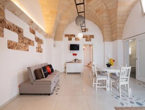 Un'ampia zona giorno con un divano, un tavolo da pranzo con sedie, una TV a parete e un arco in pietra.