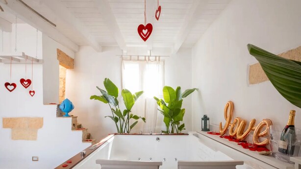 A modern bathroom with a bathtub, potted plants, and decorative elements like heart-shaped balloons and a 'Love' sign. - Petra Domus Spa & Private Lodge (Veglie)