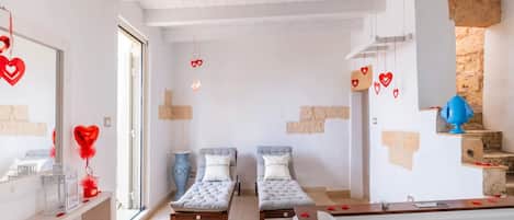 A room with two single beds, a wooden bench, a small table with a vase, and a ceiling fan.