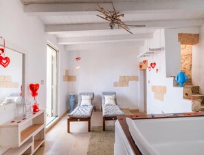 Ein Zimmer mit zwei Einzelbetten, einer Holzbank, einem kleinen Tisch mit einer Vase und einem Deckenventilator.