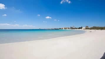 Una playa con aguas azules cristalinas, una orilla arenosa y edificios al fondo.