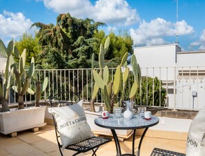 A terrace with a table set for two, surrounded by cacti, a white fence, and a building in the background. - Petra Domus Spa & Private Lodge (Veglie)
