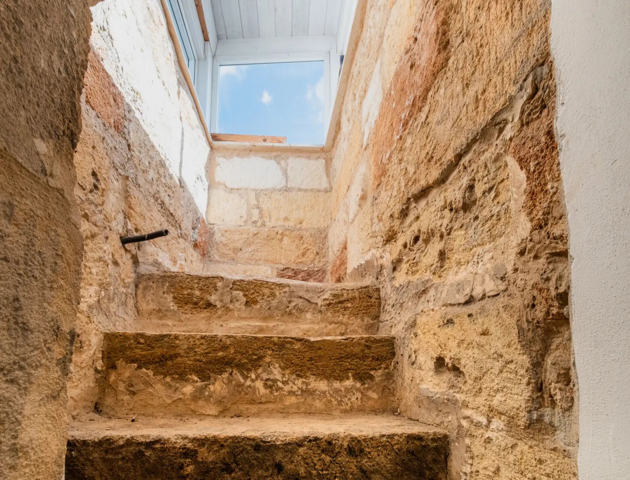 A narrow stone staircase with a skylight at the top.