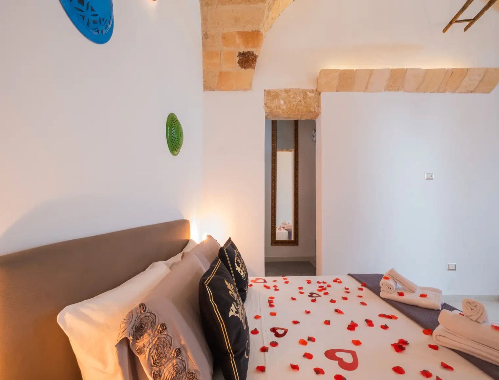 Una camera da letto con un letto, cuscini, uno specchio e una porta che dà su un'altra stanza.